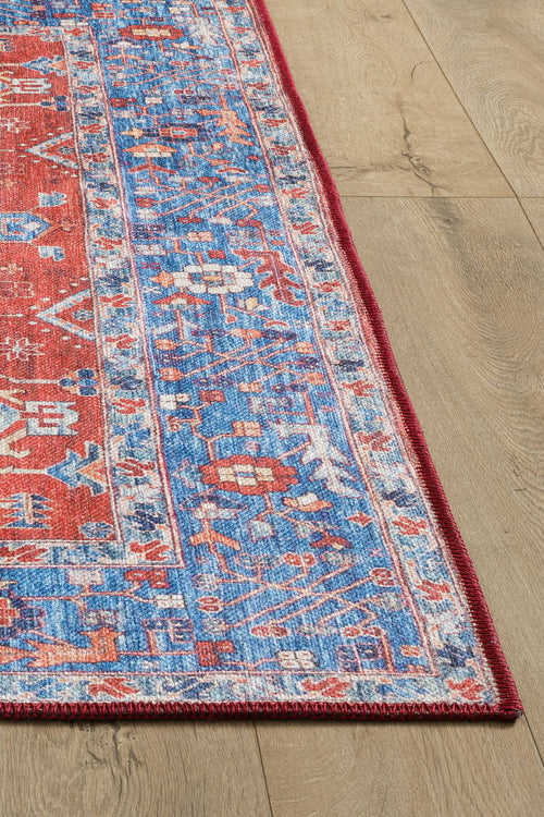 Load image 1 in gallery view. The Lunavale Red Blue Washable Rug - LCC3007 features a detailed blue pattern on red, bordered by red trim, shown on a light wood floor—perfect for high-traffic areas and easy to clean.