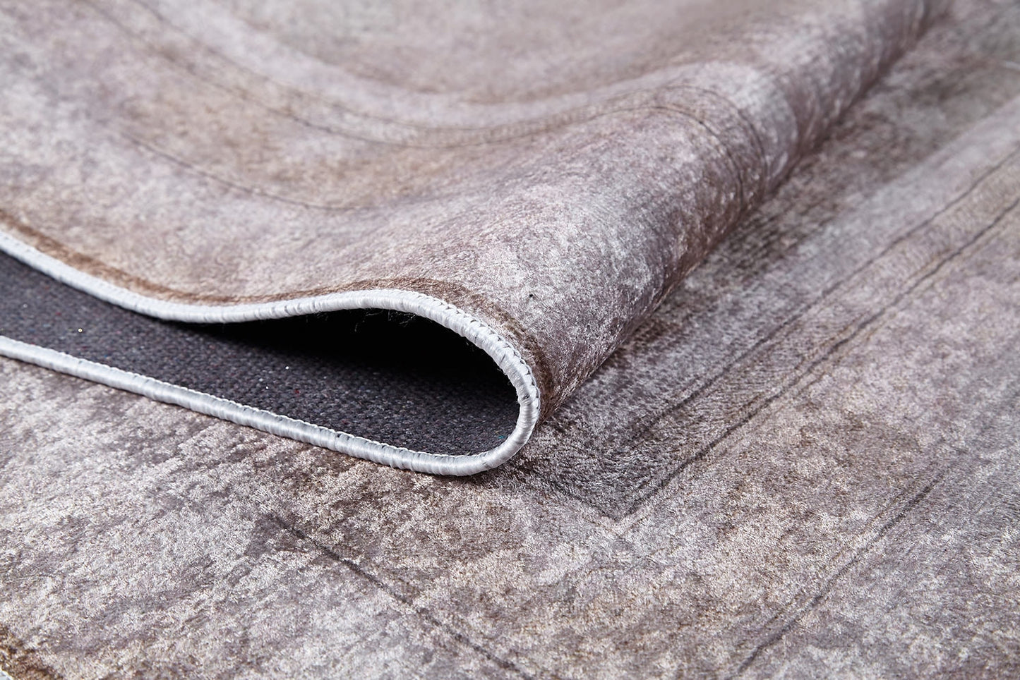 A close-up of the Luxe Borderline - Washable Rug - JR1741 (Custom Size) shows its curled corner, surface pattern, and stitched edges. In muted bronze and brown tones, it’s ideal for high-traffic areas and easy to clean.
