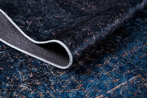 Load image 1 in gallery view. A close-up of the Luxurious Fleur - Washable Rug - JR1897 (Custom Size) in dark blue and black with a folded corner reveals its textured underside. The rug boasts an intricate, distressed brown and blue design, perfect for high-traffic areas.