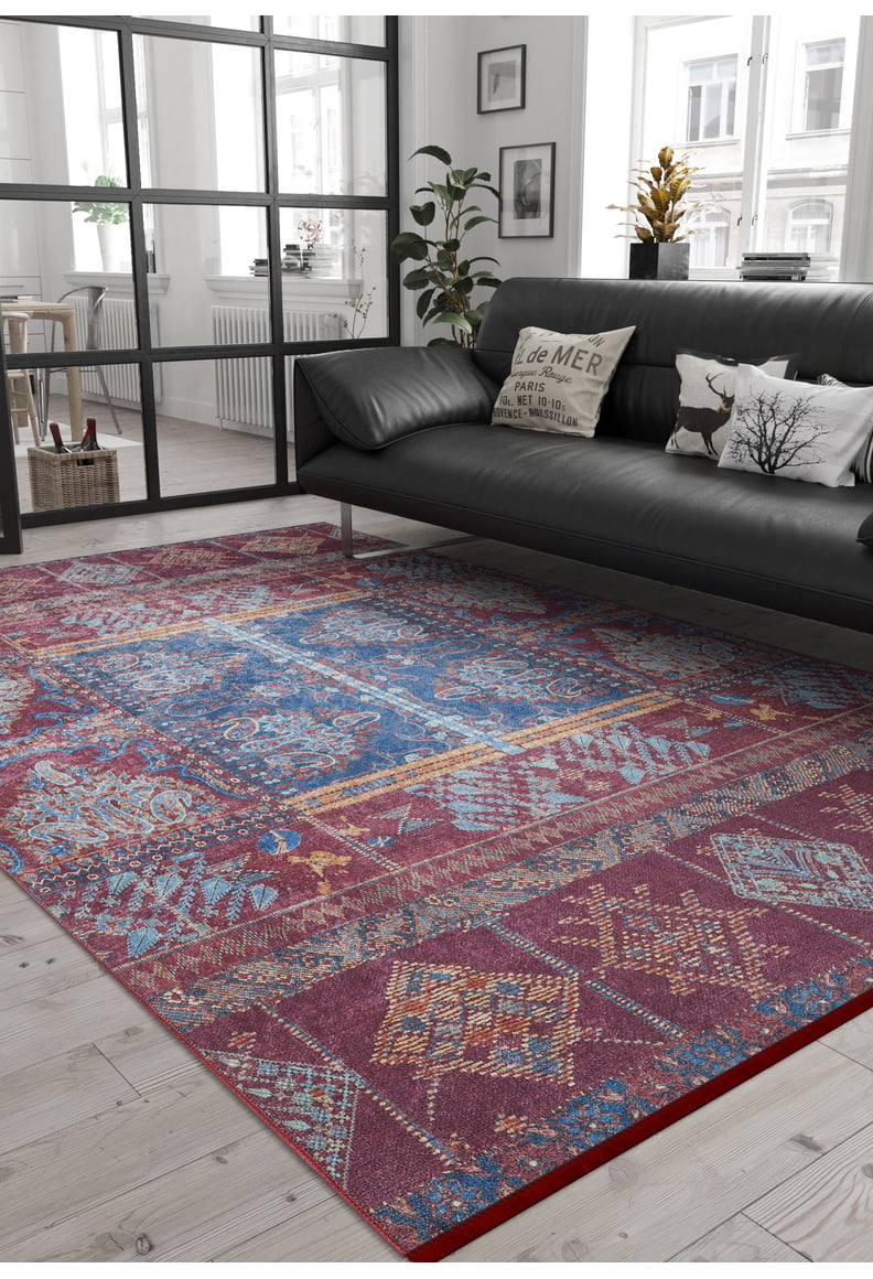 A modern living room with a black sofa, decorative pillows, a potted plant, and the Majestic Mandarin - Washable Rug - JR1863 (Custom Size) in red, blue, and yellow on light wood floors—ideal for busy spaces. Glass doors divide the rooms.