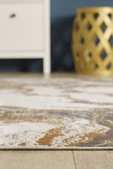 A close-up of the Majestic Marble Premium Area Rug - M673M, featuring brown, beige, and blue tones on a wooden floor. A white cabinet and a yellow decorative lattice stool are visible in the background.