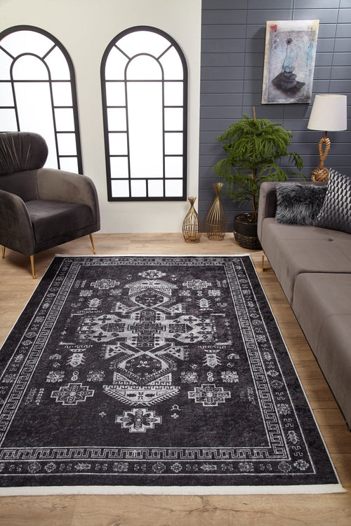 Load image 1 in gallery view. A modern living room features wood flooring, a gray sofa, black armchair, indoor plants, decorative vases, large arched windows with white panes, and the Majestic Symbol - Washable Rug - JR1892 (Custom Size) on the floor beneath a painting.