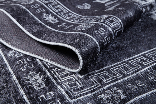 Load image 1 in gallery view. A close-up of the Majestic Symbol - Washable Rug - JR1892 (Custom Size) in black with white geometric and floral patterns, highlighting its folded edge to reveal detailed texture, stitching, and stylish flat weave design.