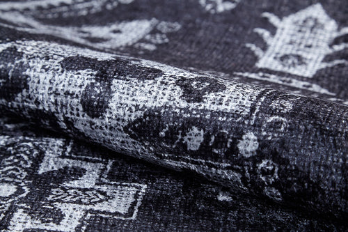 Load image 1 in gallery view. A close-up of the Majestic Symbol - Washable Rug - JR1892 (Custom Size) shows its flat weave fabric in black, gray, and white with a faded geometric pattern. The partially rolled rug highlights its intricate design and textured surface.