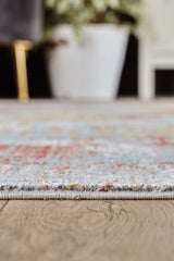 Close-up of the Medallion Remix Colorful Premium Rug - MT120 on a wooden floor, focusing on its vibrant edge. In the blurred background, a white plant pot with green foliage and part of a chair are visible.