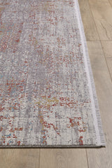 A close-up of the Medallion Remix Colorful Premium Rug - MT120 features an abstract pattern in gray, red, yellow, and blue with a white fringe, displayed on a light wood floor.
