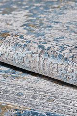 A close-up of the Medallion Revamp Modernised Medallion Rug - MT002, rolled up to show its textured, abstract pattern in blue, gray, ivory, and gold. The soft surface features a slightly raised design.