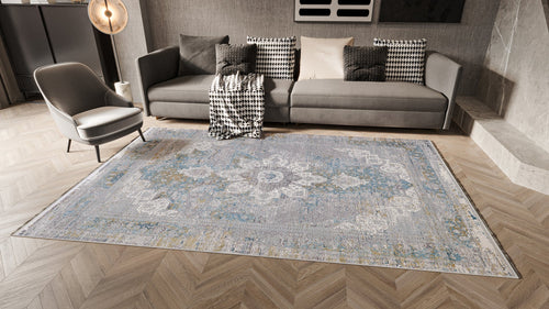 Load image 1 in gallery view. A modern living room with a grey sofa, assorted cushions, a patterned throw, grey armchair, round floor lamp, and the Medallion Revamp Modernised Medallion Rug - MT002 featuring blue, white, and gold accents on herringbone wood floors.