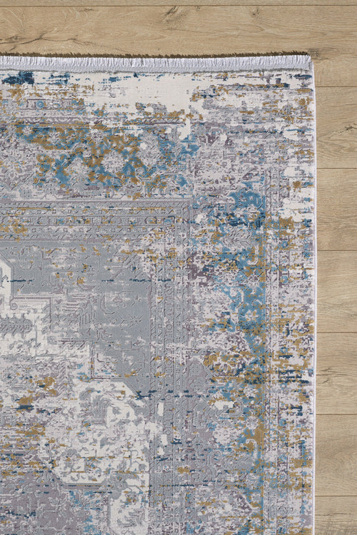 Load image 1 in gallery view. A section of the Medallion Revamp Modernised Medallion Rug - MT002, in blue, gold, gray, and white with a distressed abstract design and fringed edge, lies on a light wood floor.