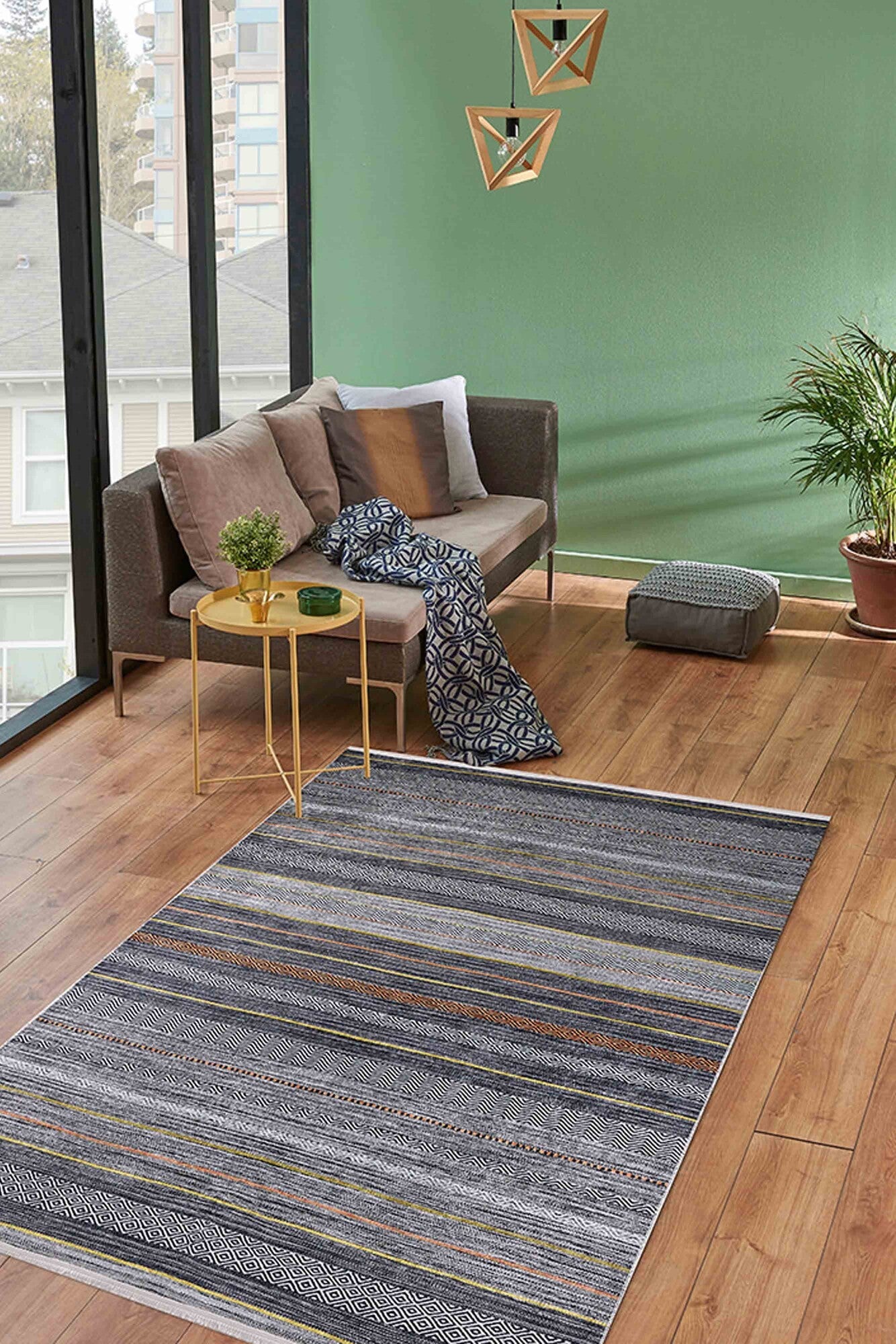 A modern living room with a green accent wall, brown sofa, gold side table with plant, and the Metro Lines - Washable Rug - JR1548 (Custom Size) in gray-anthracite on wood floors, plus large windows letting in natural light.