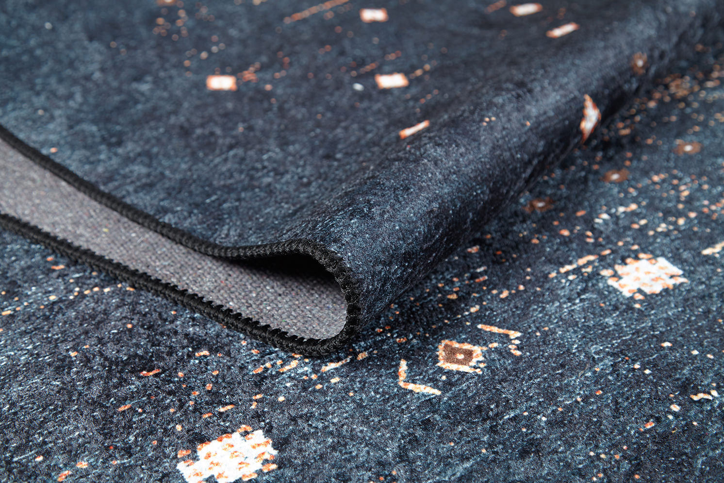 A close-up of the Midnight Majesty - Machine-Washable Rug (JRS5052, Custom Size) in dark blue, featuring a folded corner that highlights its textured surface and intricate white and light brown geometric patterns—ideal for high-traffic areas.