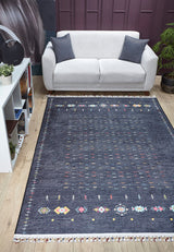 A modern living room with a light gray sofa, two dark cushions, the Midnight Majesty machine-washable rug (JRS5052) featuring colorful accents—perfect for high-traffic areas—a white shelving unit with plants and books, and a potted plant in the corner.