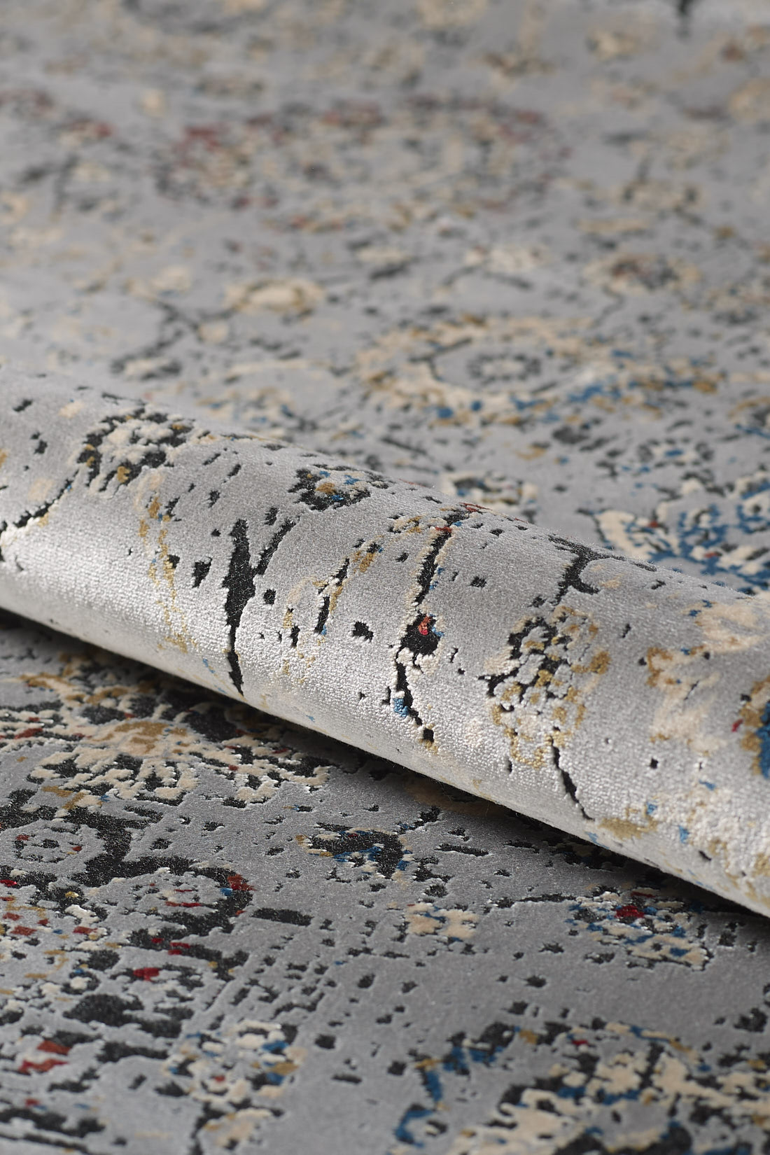 A close-up of the Miniature Elegance Oushak Rug - Grey - 2084F, a machine-made modal silk-polyester rug with an abstract floral pattern in beige, blue, black, and red. Its soft texture is slightly raised in select areas.