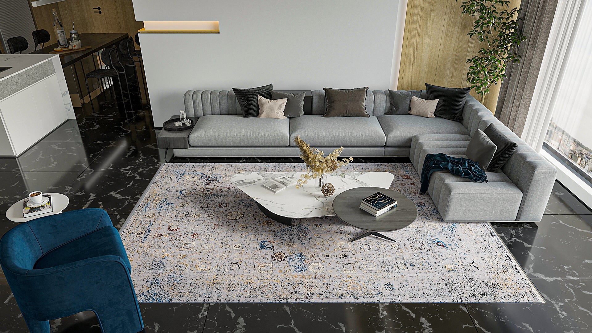 Modern living room with a large gray sectional, assorted pillows, a round marble coffee table, blue armchair, and the Miniature Elegance Oushak Rug - Grey - 2084F on black marble floors. Large plant and kitchen in the background.
