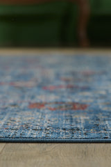 A close-up, low-angle view of the Miniature Elegance Oushak Rug - Navy - 2084E, featuring blue tones with red and beige accents in its woven design, displayed on a wooden floor with a blurred green background.