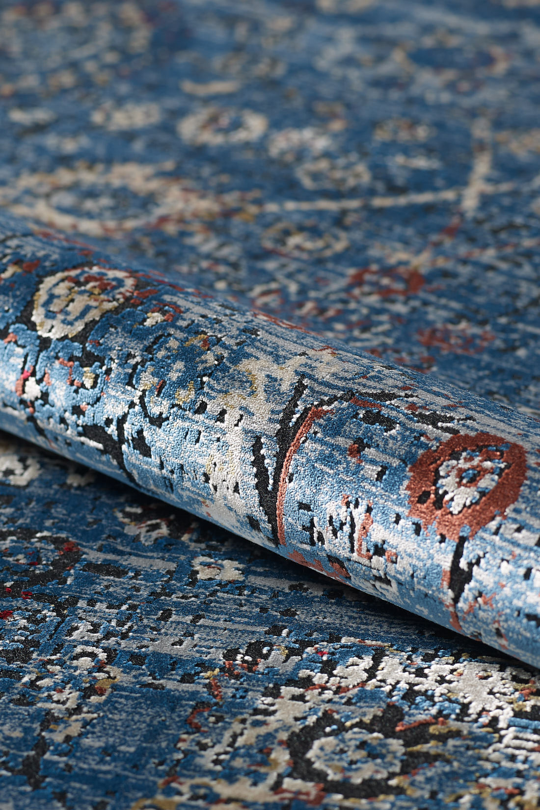 A close-up of the Miniature Elegance Oushak Rug - Navy - 2084E, a machine-made blue modal silk rug with intricate white, red, and beige patterns, highlights its textile texture and vibrant colors laid on a matching surface.