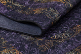 A close-up of the Minimalist and Elegant - Washable Rug - JR1298 shows its intricate gold, purple, and orange patterns. Partially folded to reveal a textured underside, this custom-size rug is perfect for high-traffic areas.