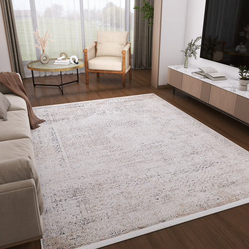 Load image 1 in gallery view. A modern living room features the Misty Mosaic - Washable Rug - JR1690 with a light pattern, paired with a beige sofa, wooden armchair, round decor coffee table, and a TV console accented by books, plants, and ample natural light from floor-to-ceiling windows.