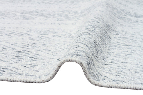 Load image 1 in gallery view. A close-up of the Modern Mist - Washable Double-Sided Kilims - AR01 rug, slightly lifted to reveal its texture, thickness, visible edge stitching, and a subtle pattern that enhances its modern style.