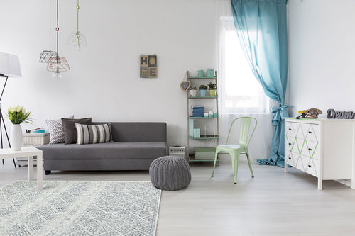 Load image 1 in gallery view. Modern living room featuring a gray sofa, Modern Mist - Washable Double-Sided Kilims - AR01 rug, white table, pouf, metal chair, geometric cabinet, shelves with plants, blue curtains, minimalist art on walls, and hanging lights.
