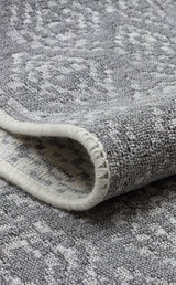 Close-up of the Modern Mist - Washable Double-Sided Kilims - AR01, a folded grey rug with a subtle geometric pattern and visible edge stitching, highlighting its contemporary style and quality craftsmanship.