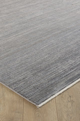 A close-up of the Muted Palette Grey Ombre Rug - EW2636, a modern machine-made piece with subtle linear patterns and a fringed edge, displayed on a light wooden floor in elegant neutral tones.