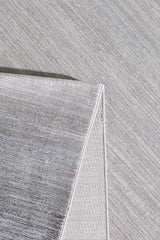 A close-up view of the Muted Palette Grey Ombre Rug - EW2636 shows its textured surface with a folded corner, highlighting the weave and subtle color variations in this modern, light grey neutral-toned rug.