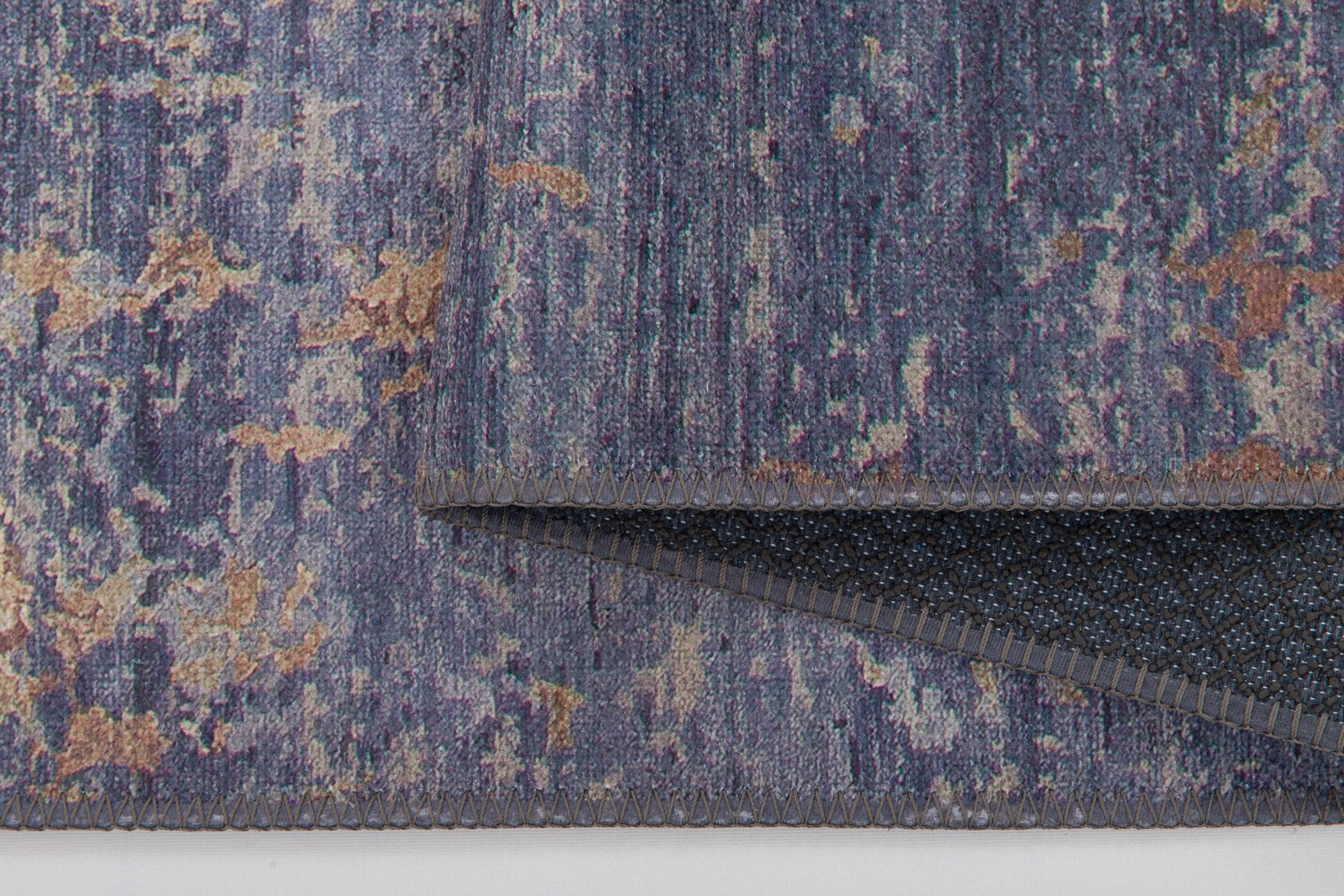 A close-up of the Mystical Mosaic - Washable Rug - JRS003 (Outlet) US in blue, purple, beige, and brown highlights its textured surface, neat stitching, folded corner, and black non-slip underside—perfect for high-traffic areas.