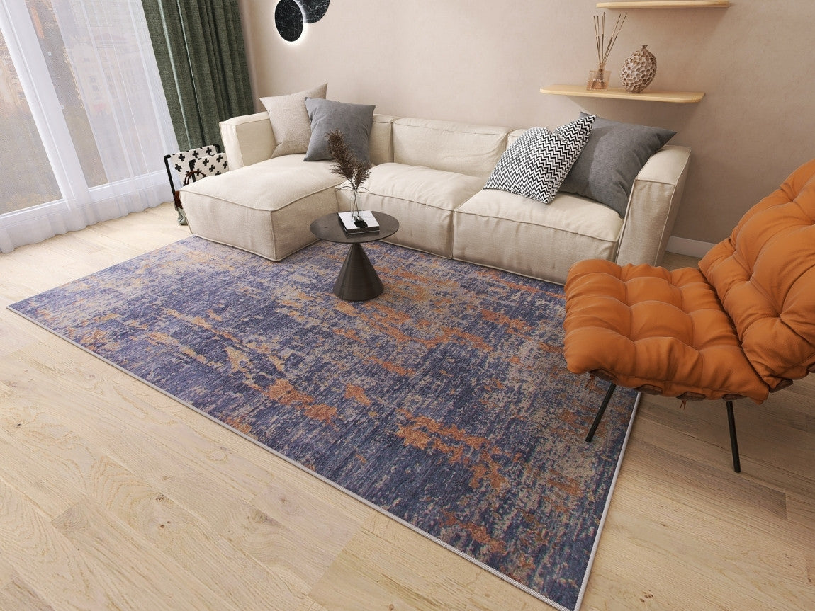 A modern living room featuring a beige sectional, orange lounge chair, small black coffee table, and the Mystical Mosaic - Washable Rug - JRS003 (Custom Size) in blue and orange—ideal for high-traffic areas. Light wood floors, shelves, and pillows complete the minimal decor.