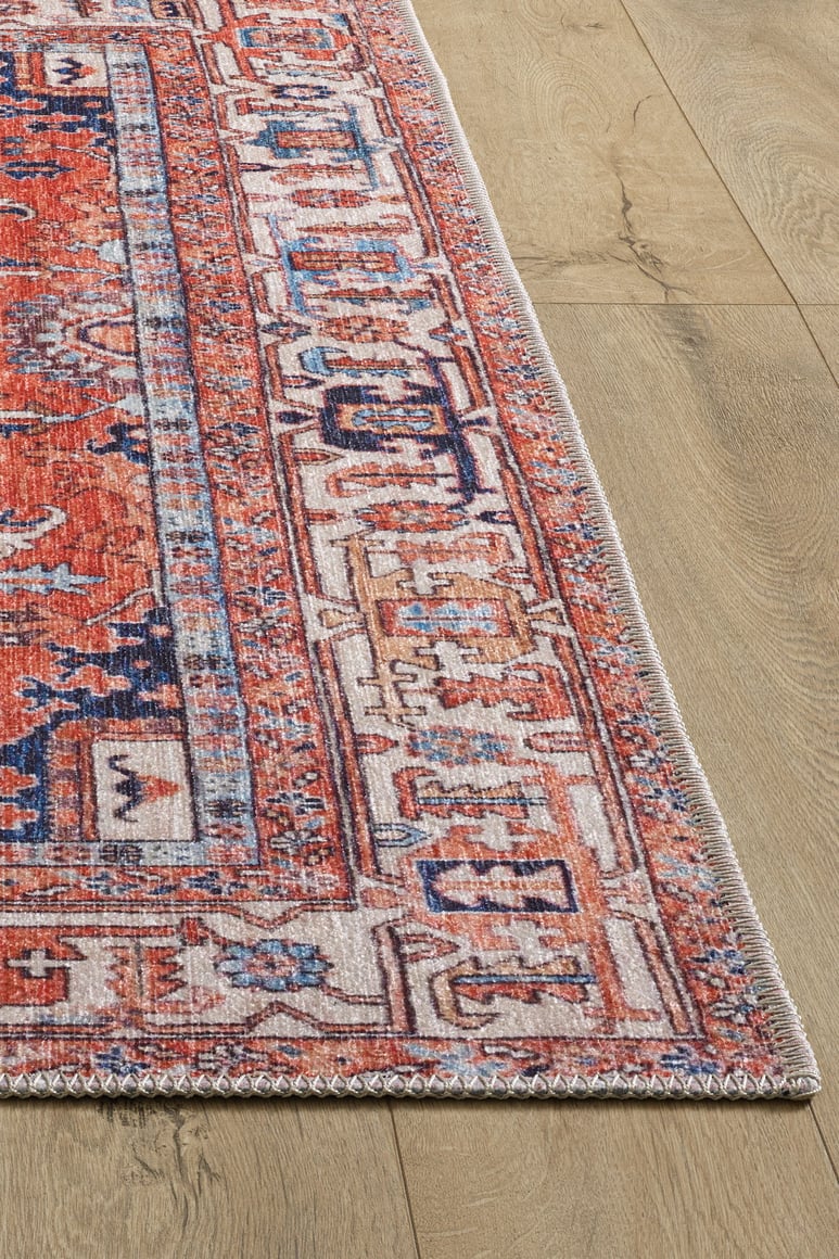 A close-up of the Mystral Kilim-Design Coral Washable Rug (LCC3015) shows its red, blue, and ivory geometric pattern on a light wood floor. The image highlights the rug’s corner and detailed border—ideal for high-traffic areas.