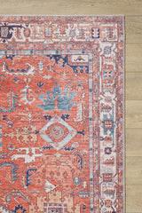A close-up of the Mystral Kilim-Design Coral Washable Rug - LCC3015, showing its intricate red, blue, and cream geometric patterns—ideal for high-traffic areas. Only a corner of this colorful rug is visible on a light wooden floor.