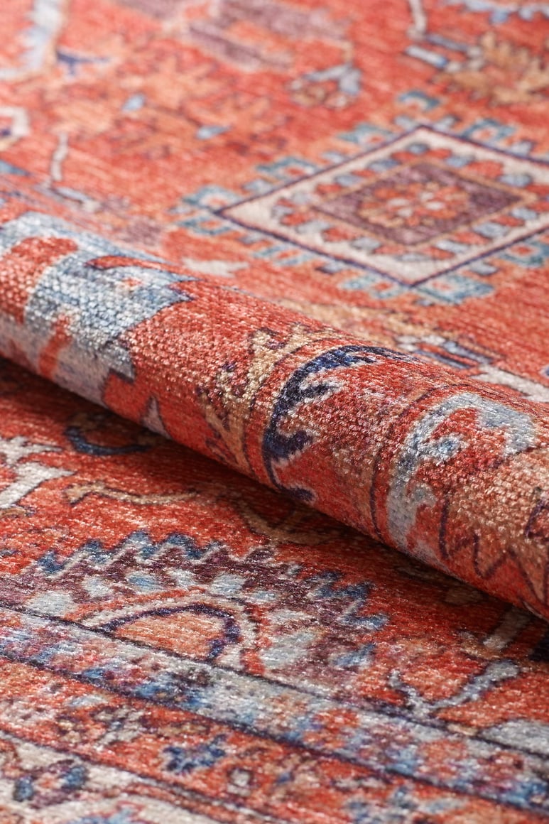 A close-up of the Mystral Kilim-Design Coral Washable Rug - LCC3015 (Custom Size) rolled up, shows its intricate red, white, blue, and gold geometric patterns—ideal as a washable rug for high-traffic areas.
