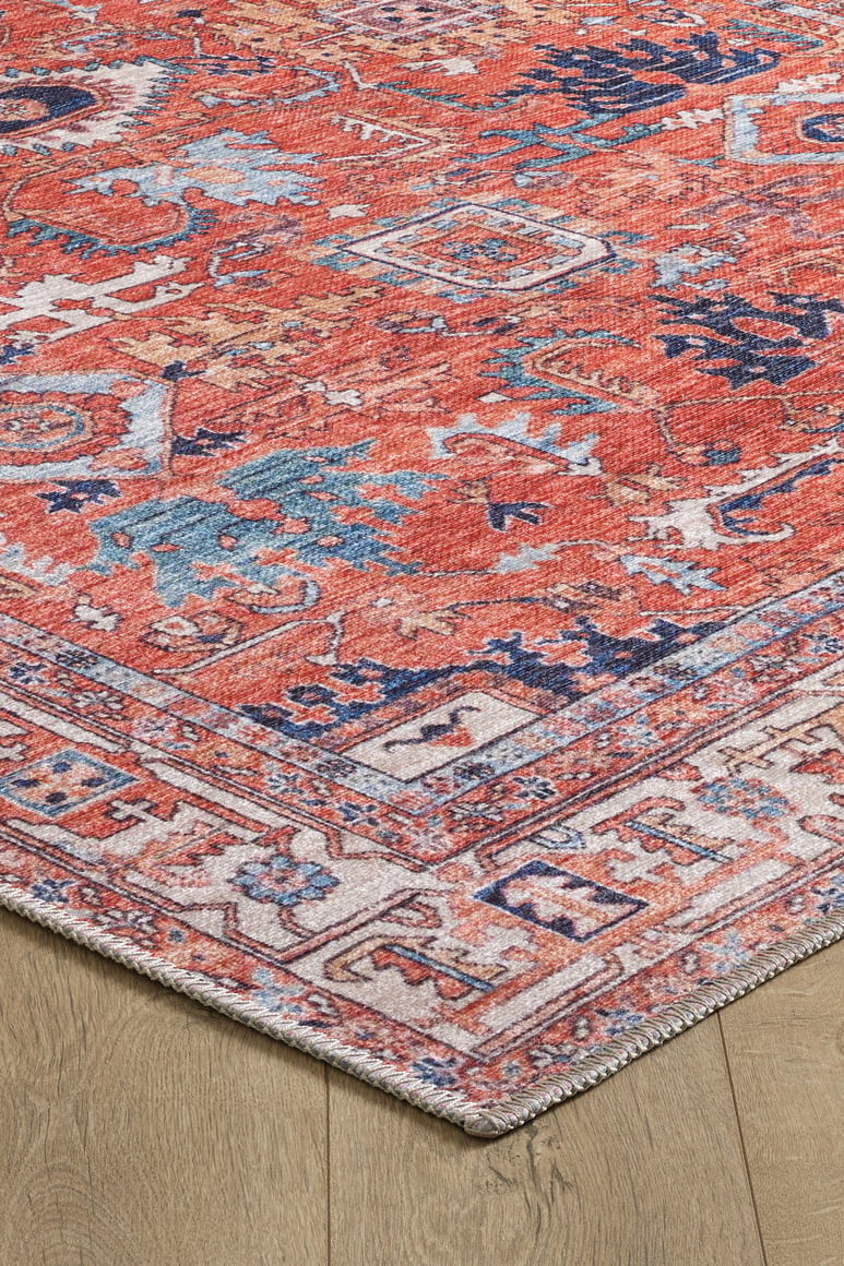 A close-up of the Mystral Kilim-Design Coral Washable Rug - LCC3015 (Custom Size) shows its rectangular, multicolored geometric and floral patterns in red, blue, and cream on a light wooden floor—ideal for high-traffic areas.