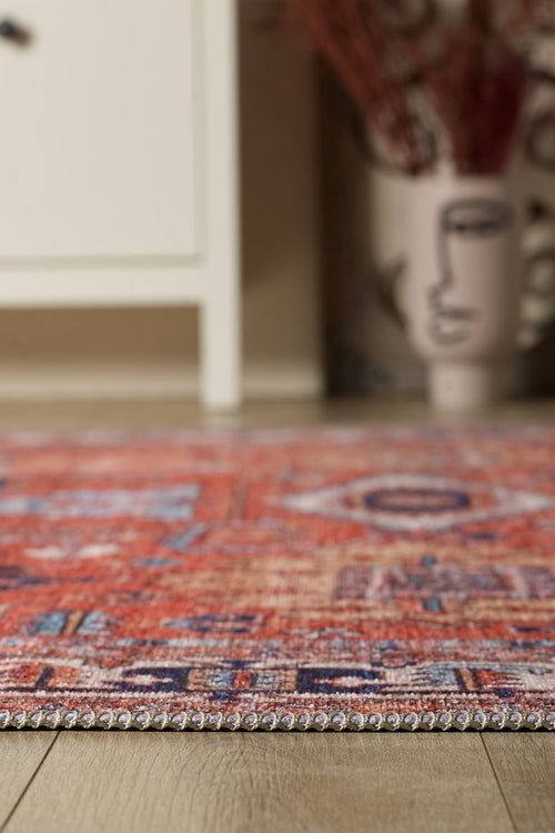 Load image 1 in gallery view. A close-up of the Mystral Kilim-Design Coral Washable Rug - LCC3015 (Custom Size) on a wooden floor, ideal for high-traffic spaces, with a blurred white cabinet and abstract face vase in the background.