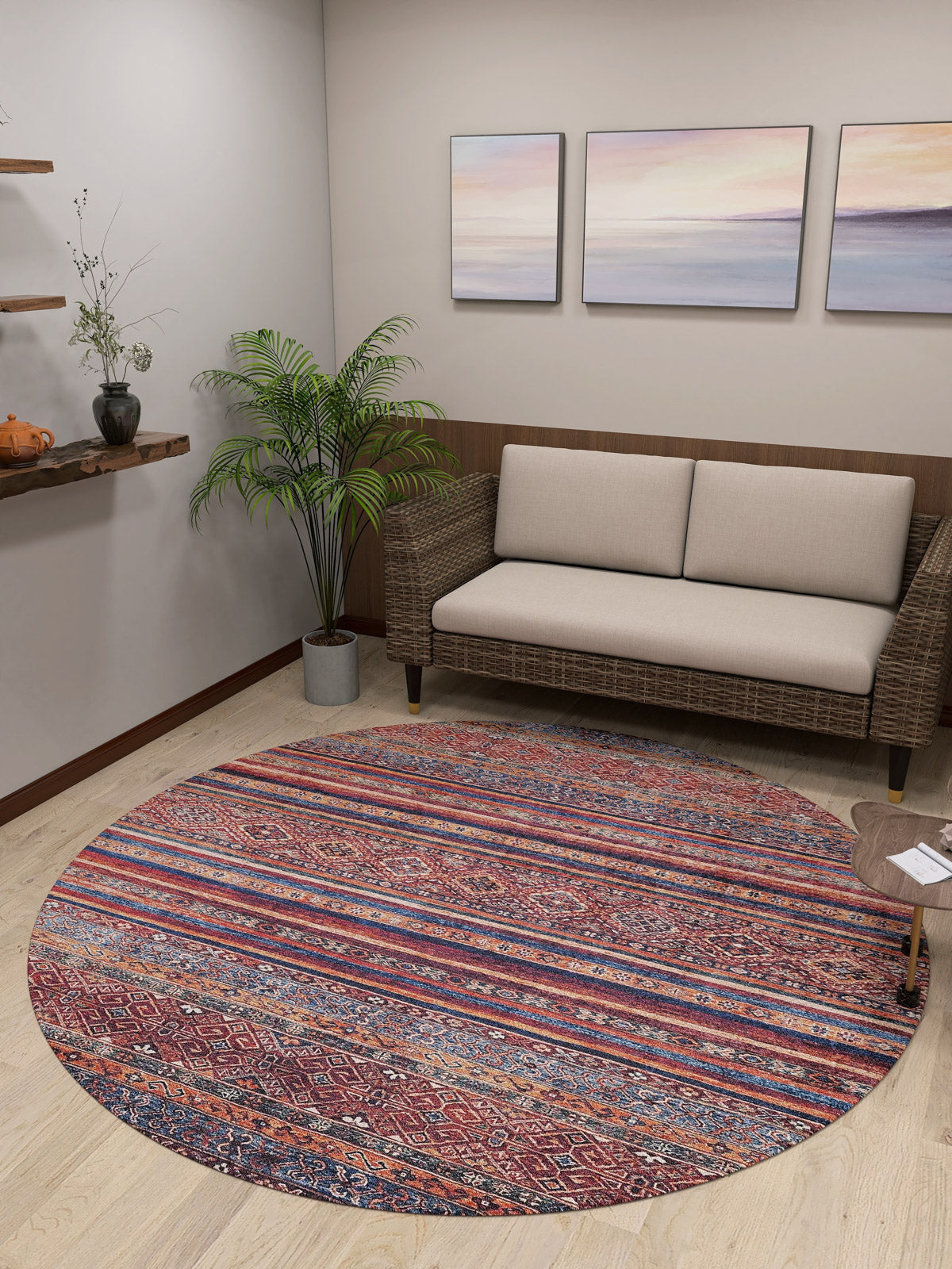 A cozy living room features the Native Nightscape - Washable Rug - JR5093, ideal for high-traffic areas, a wicker loveseat with cream cushions, a potted plant, pastel landscape wall art, and a floating shelf with charming accents.