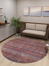 A cozy living room features the Native Nightscape - Washable Rug - JR5093, ideal for high-traffic areas, a wicker loveseat with cream cushions, a potted plant, pastel landscape wall art, and a floating shelf with charming accents.