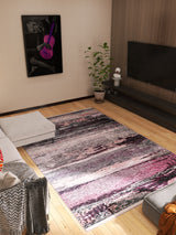 A modern living room with the Natural Brushed - Washable Rug - JR336 (Custom Size) in pink, gray, and black on wood floors, alongside a sectional sofa, potted plant, TV on a wood-paneled wall, and purple guitar artwork—perfect for high-traffic areas.