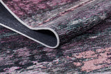 A close-up of the Natural Brushed - Washable Rug - JR336 (Custom Size) in multicolored pink, purple, black, and white tones shows a lifted corner to highlight its texture and stitching—ideal for stylish, high-traffic areas.