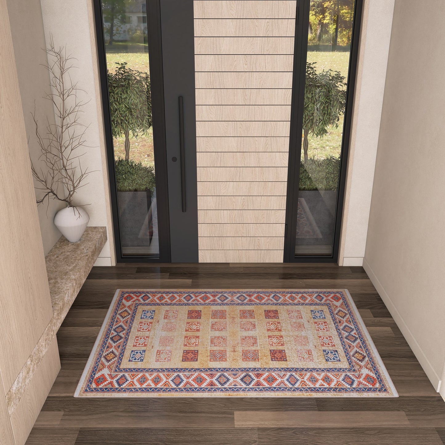 The Navajo Nights - Washable Rug - JR1758, with its colorful geometric pattern, decorates a modern entryway featuring light walls, a marble bench with a white vase and bare branches, and a large glass door—ideal for high-traffic areas.