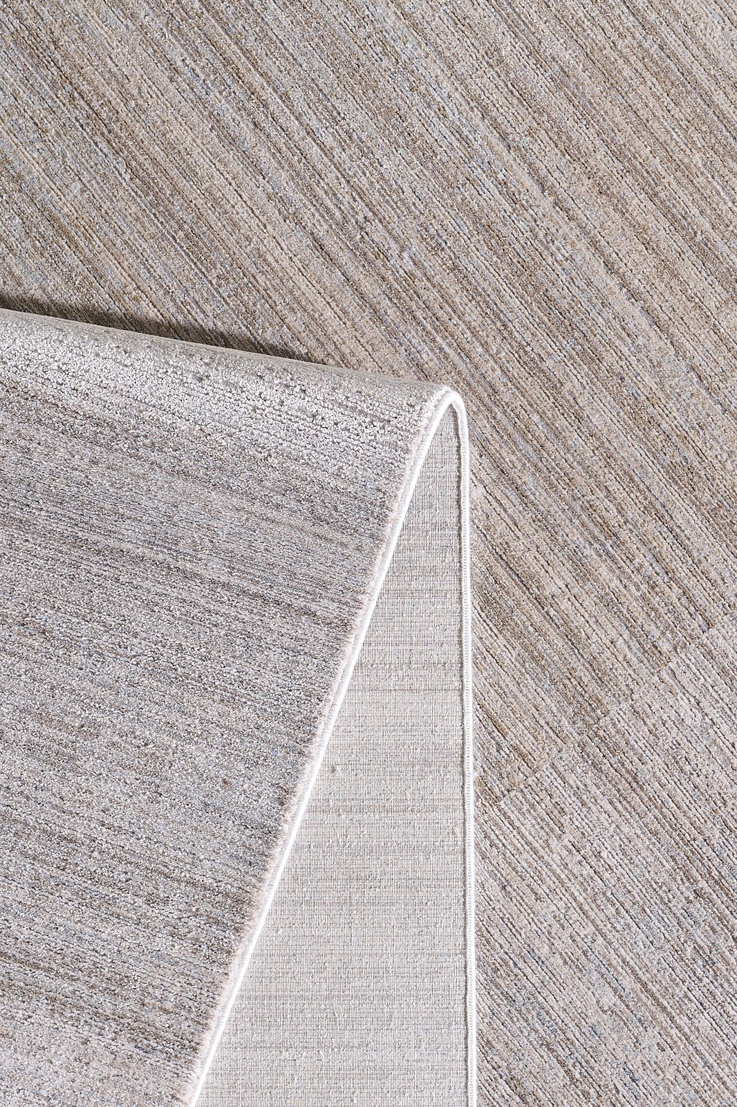A close-up of the Neutral Frame Modern Bordered Rug - EW5541 with one corner folded over, showing both the front and underside of this neutral-colored, machine-made rug against a matching background.
