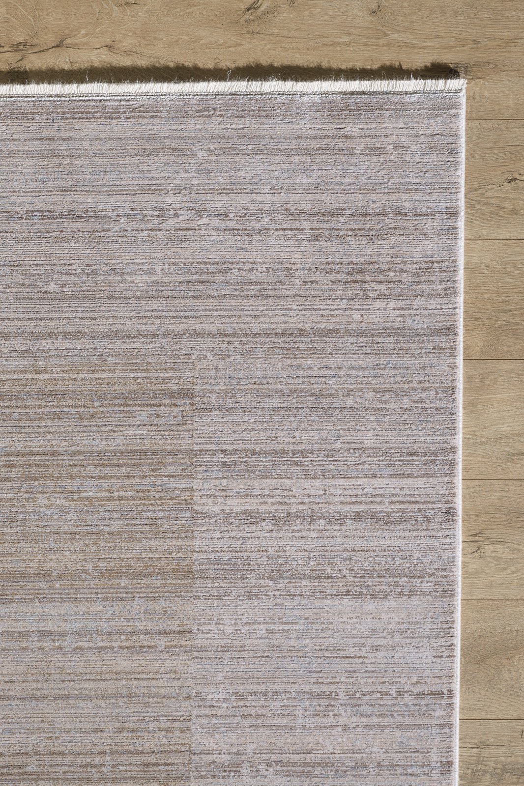 A close-up of the Neutral Frame Modern Bordered Rug - EW5541 shows its textured, light beige surface and fringe edges, elegantly placed on a light wood floor.