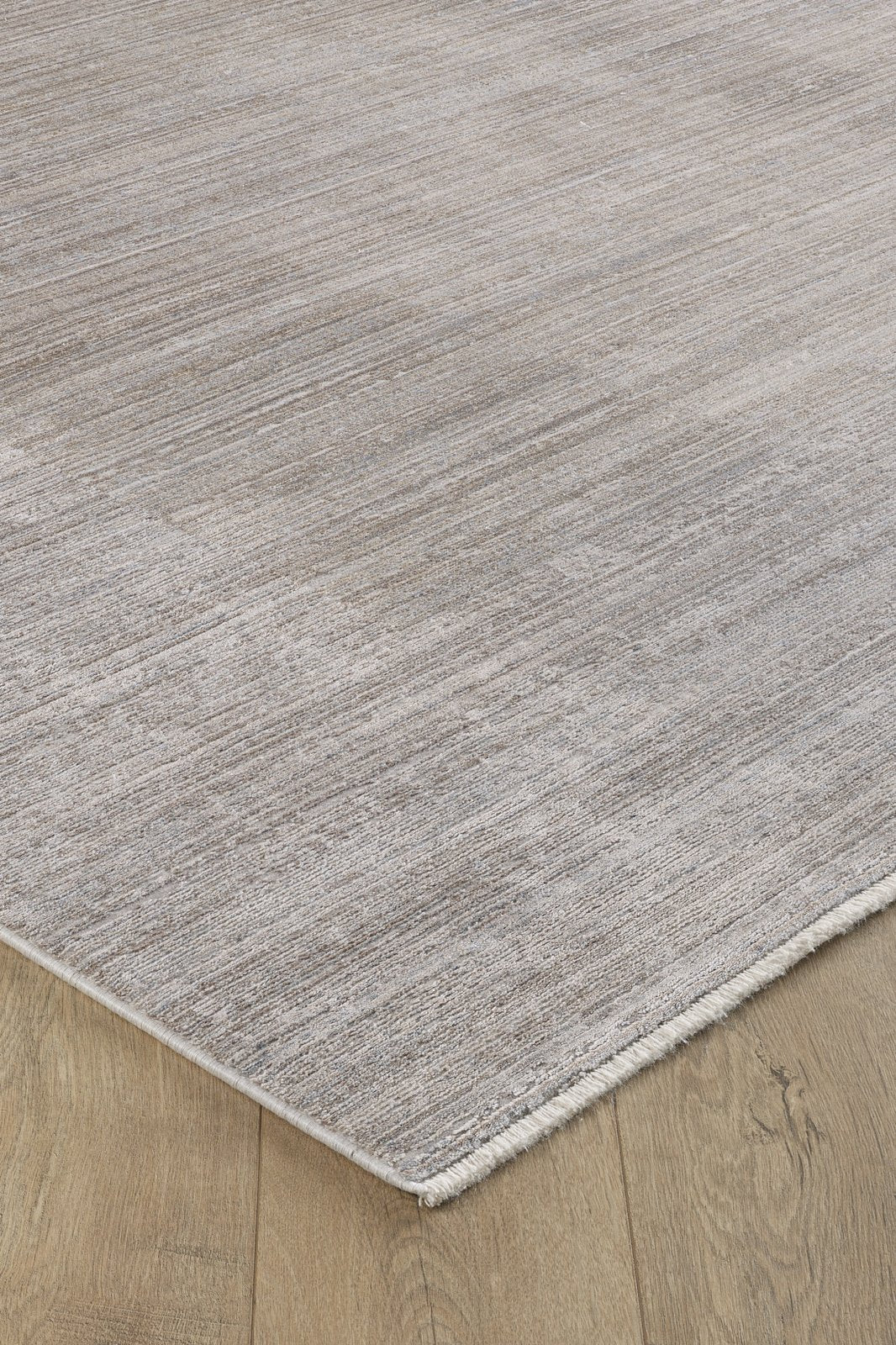 A close-up of the Neutral Frame Modern Bordered Rug - EW5541, featuring a minimalist light grey texture and fringed edges, displayed on a wooden floor with a natural oak finish.