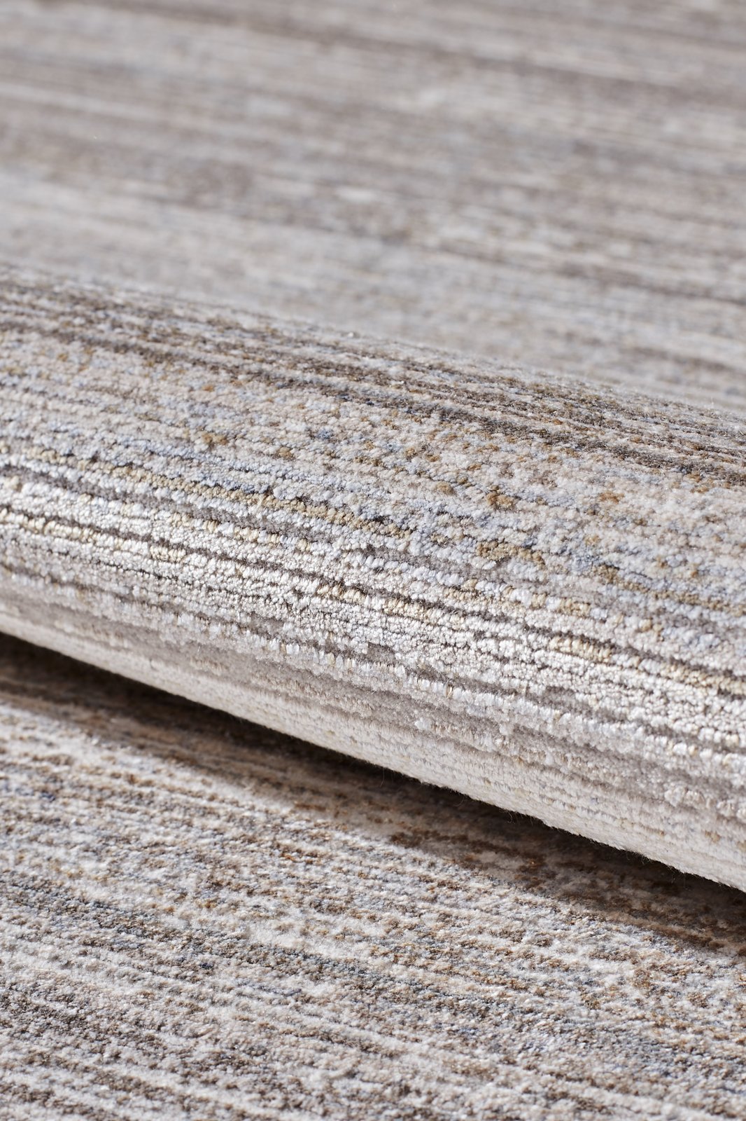 A close-up of the Neutral Frame Modern Bordered Rug - EW5541 shows its soft, slightly shiny surface and rolled, textured design with striped beige, gray, and cream tones.