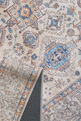 The Nexa Bordered Beige Washable Rug - LCC3009 is a flat weave rug with intricate geometric and floral patterns in blue, orange, and beige tones. One corner is folded to show its textured, non-slip backing.