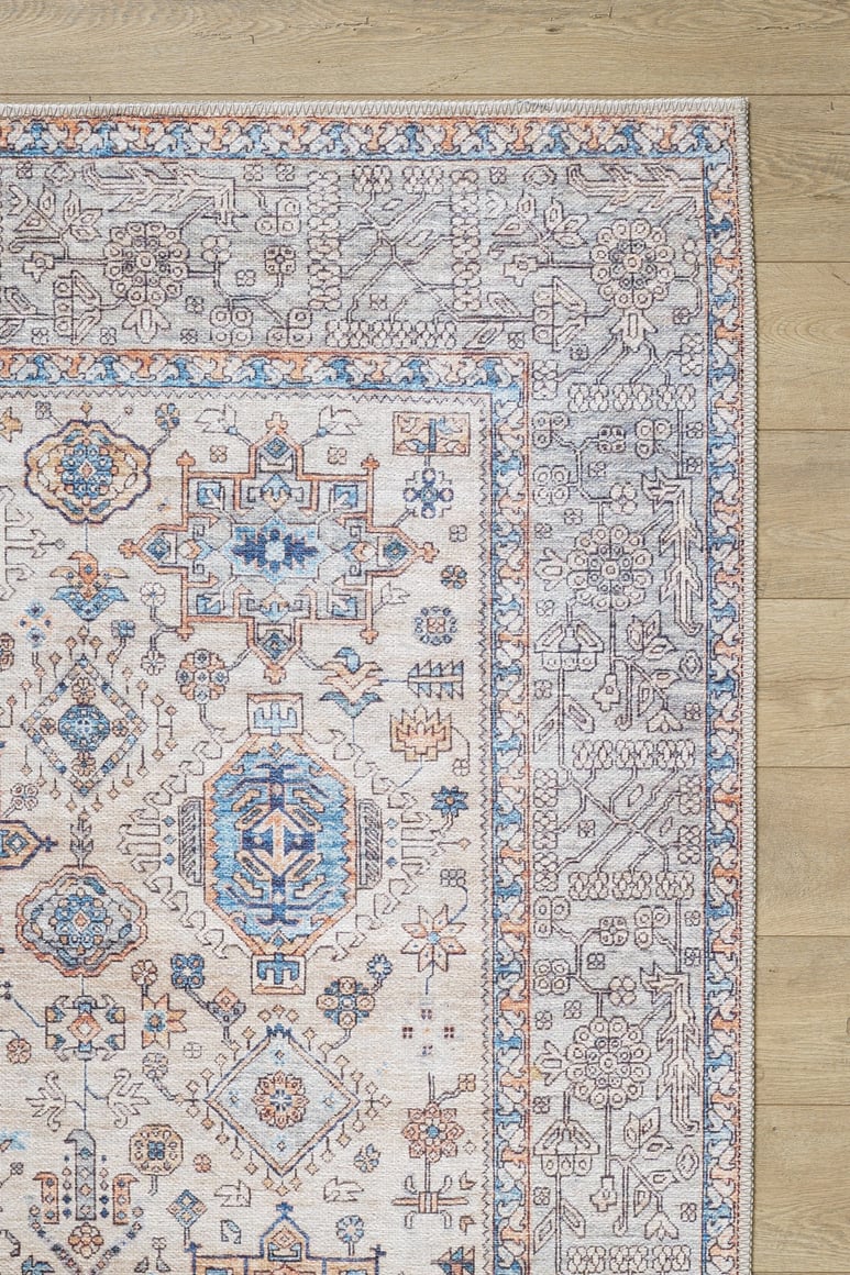 A close-up of the Nexa Bordered Beige Washable Rug - LCC3009 (Custom Size) highlights its blue, orange, and gray geometric-floral patterns on a beige background—an ideal choice for high-traffic areas on light wood floors.