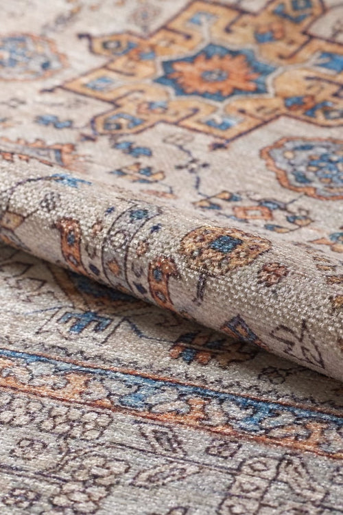 Bild 1 in Galerieansicht laden. A close-up of the Nexa Bordered Beige Washable Rug - LCC3009 (Custom Size), showing intricate floral and geometric patterns in beige, blue, gold, and brown, with a folded edge highlighting its texture—ideal for high-traffic spaces.