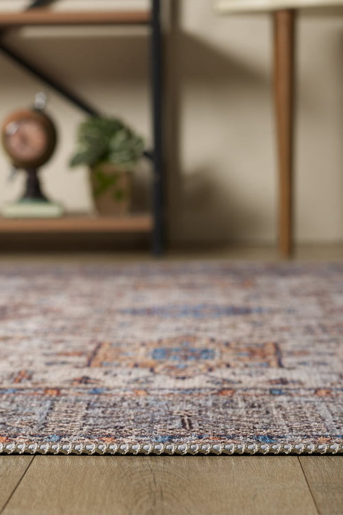 Bild 1 in Galerieansicht laden. A close-up of the Nexa Bordered Beige Washable Rug - LCC3009 (Custom Size) on a wooden floor, ideal for high-traffic areas, with a shelf in the background holding a globe and potted plant, plus part of a table with wooden legs.