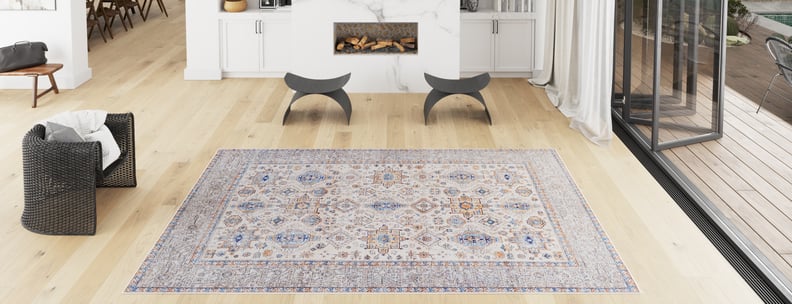 A bright, modern living room with light wood floors, a Nexa Bordered Beige Washable Rug - LCC3009 (Custom Size), a black woven chair, curved gray stools, a fireplace, and large windows—ideal for high-traffic areas.