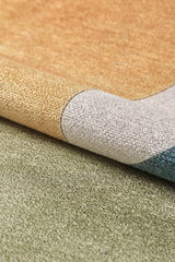 The Nexus Geometric Contemporary Washable Rug - MDJ006, in gold, gray, blue, and green tones, is shown slightly folded on a green carpet—an ideal choice for high-traffic spaces.