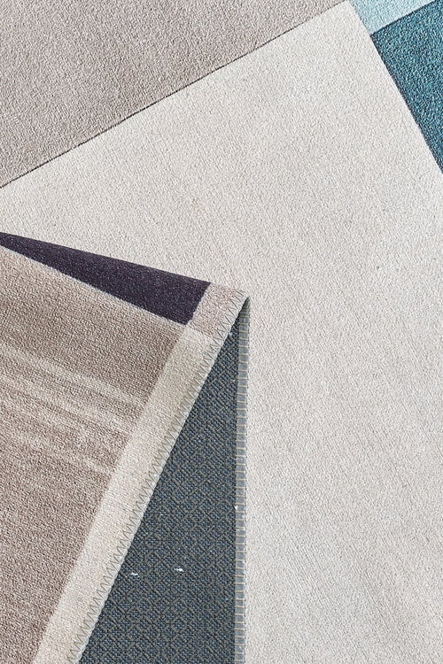 Load image 1 in gallery view. A close-up of the Nexus Geometric Contemporary Washable Rug - MDJ006 (Custom Size) shows intersecting beige, blue, and gray shapes with a flipped corner revealing its textured underside—stylish and durable for high-traffic areas.